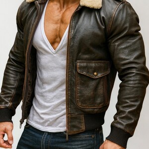 Puede incluir: Chaqueta bomber de cuero marr&oacute;n con cuello de borrego beige, cremallera frontal y dos bolsillos delanteros. La chaqueta tiene pu&ntilde;os y dobladillo de canal&eacute;. El modelo lleva una camiseta blanca con cuello en V y vaqueros azules.