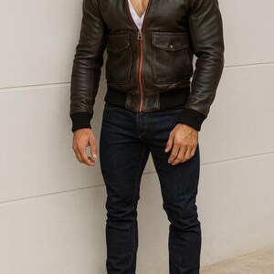 Puede incluir: Chaqueta de cuero marr&oacute;n con cuello de borrego beige, dos bolsillos delanteros y cremallera roja. La chaqueta se combina con vaqueros azul oscuro y botas de cuero marr&oacute;n. La chaqueta tiene un dobladillo y pu&ntilde;os negros acanalados.