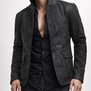 May include: A black leather jacket with a stand-up collar and button closure. The jacket has two front pockets and is worn over a black button-down shirt and black jeans. The jacket appears to be distressed.