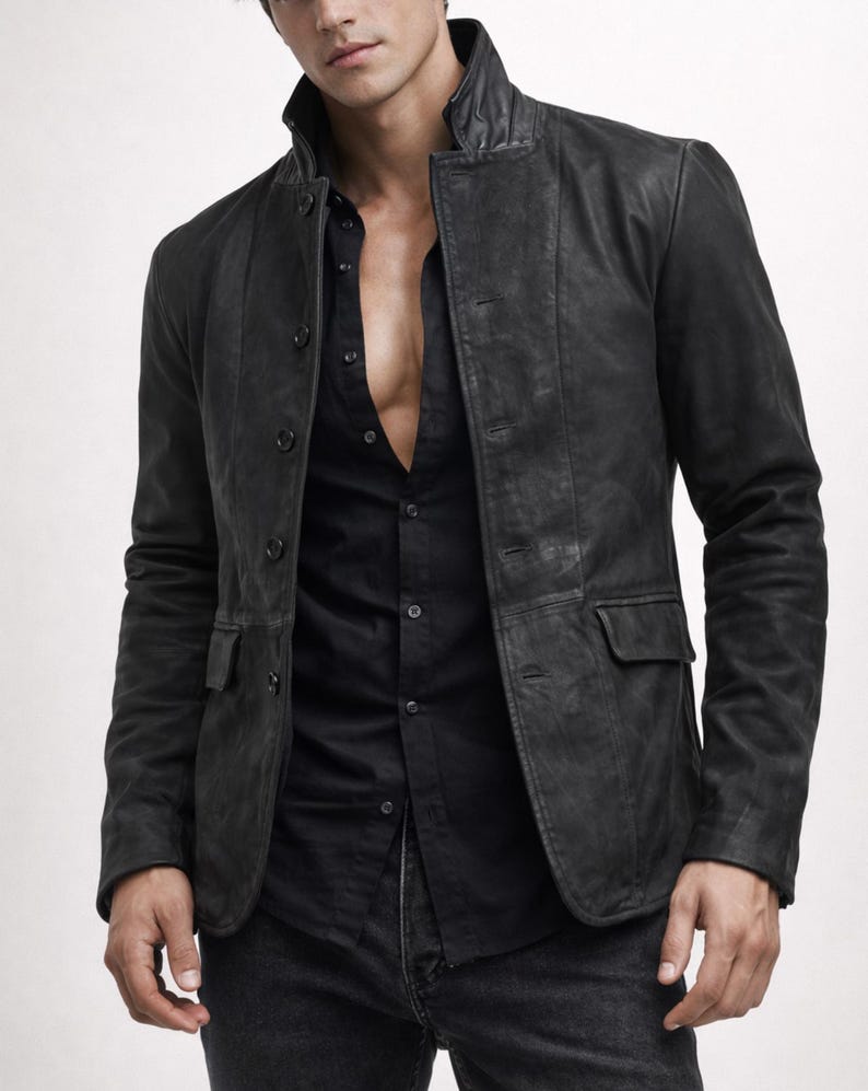 May include: A black leather jacket with a stand-up collar and button closure. The jacket has two front pockets and is worn over a black button-down shirt and black jeans. The jacket appears to be distressed.