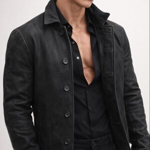 May include: A black leather jacket with a button-up front and a collared neckline. The jacket is worn over a black button-down shirt. The overall look is dark and stylish.