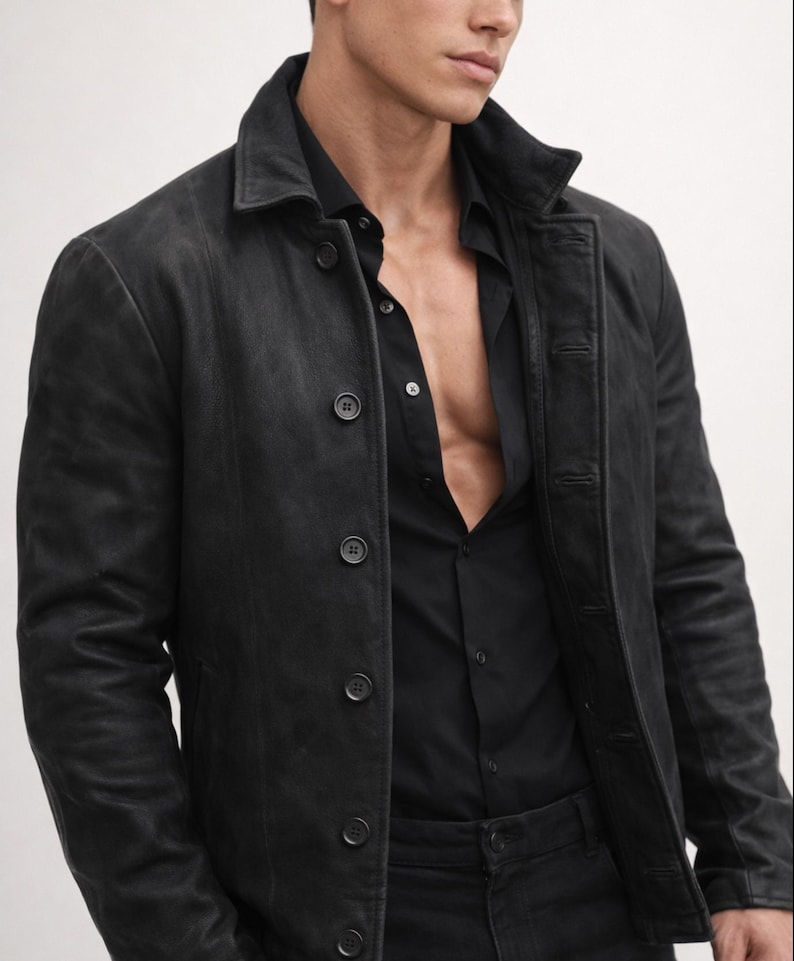 May include: A black leather jacket with a button-up front and a collared neckline. The jacket is worn over a black button-down shirt. The overall look is dark and stylish.