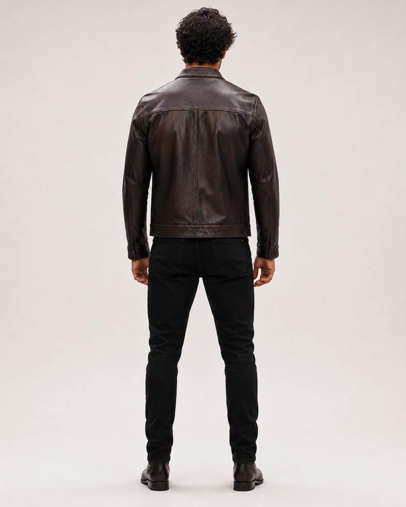 May include: A dark brown leather jacket with a classic collar, long sleeves, and a straight hemline, paired with slim-fit black trousers and dark brown leather boots, viewed from the back against a plain, neutral-coloured background.