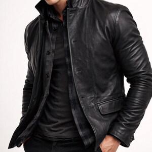 May include: A black leather jacket with a button-up front, a collar, and two front pockets. The jacket is worn over a dark shirt and a plaid shirt. The model is wearing black pants.
