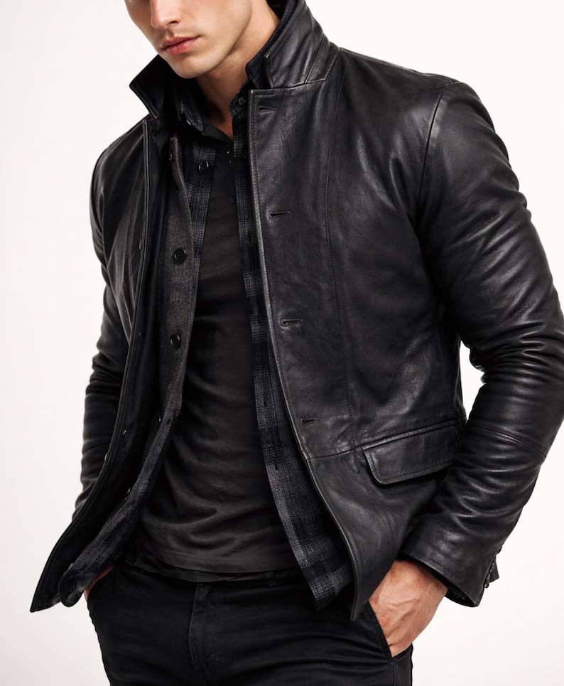 May include: A black leather jacket with a button-up front, a collar, and two front pockets. The jacket is worn over a dark shirt and a plaid shirt. The model is wearing black pants.