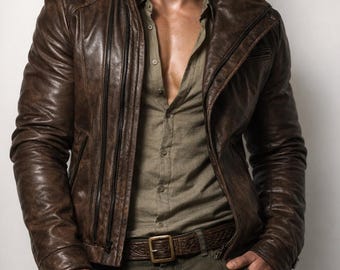 Può includere: Giacca di pelle marrone con collo alto e multiple cerniere. La giacca è indossata sopra una camicia abbottonata e abbinata a una cintura marrone e pantaloni verde oliva. La giacca sembra essere in pelle invecchiata.