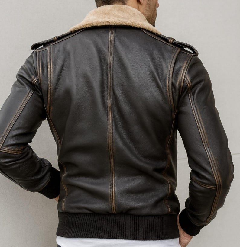 Puede incluir: Chaqueta de cuero marr&oacute;n oscuro con cuello de borrego beige. La chaqueta tiene dobladillo y pu&ntilde;os de canal&eacute;, con detalles desgastados a lo largo de las costuras y bordes. Vista trasera con charreteras.