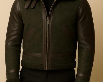 May include: A dark green leather jacket with a shearling collar and dark brown leather sleeves. The jacket has a zipper closure, two front pockets, and a shearling lining at the cuffs and hem. The jacket is a classic bomber style.
