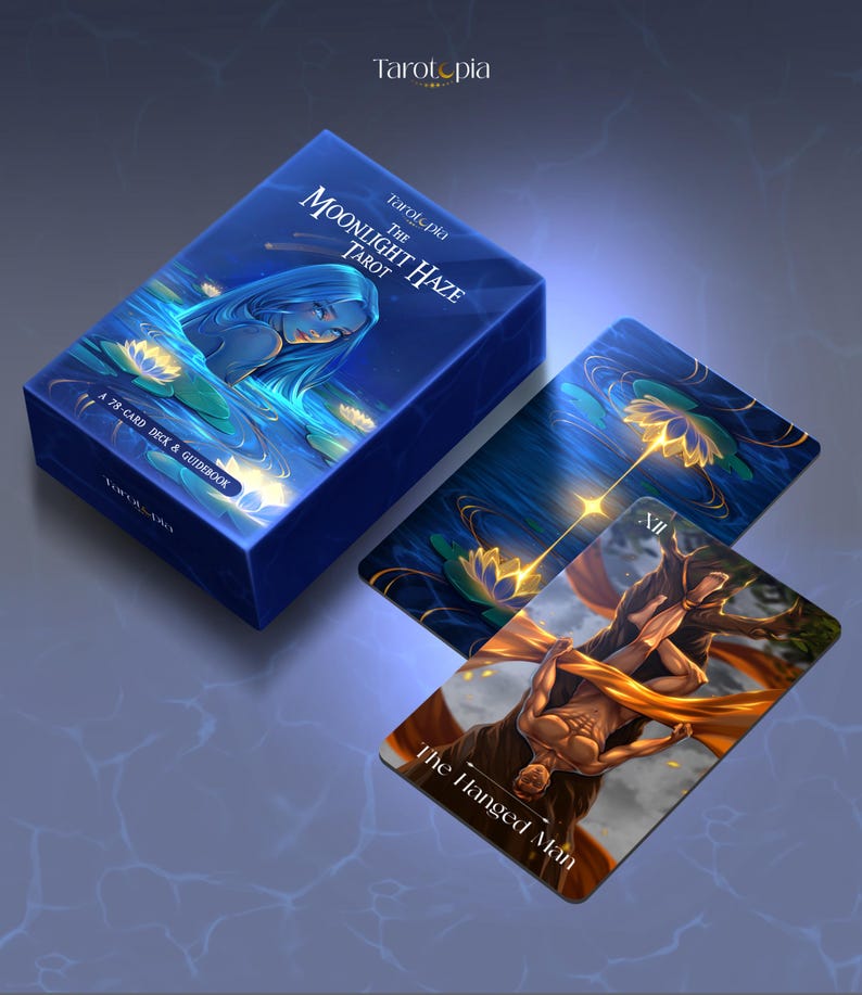May include: A blue tarot card box and cards with the text "Tarotopia" and "The Moonlight Haze Tarot". The box features an illustration of a woman in water. One card shows "The Hanged Man".