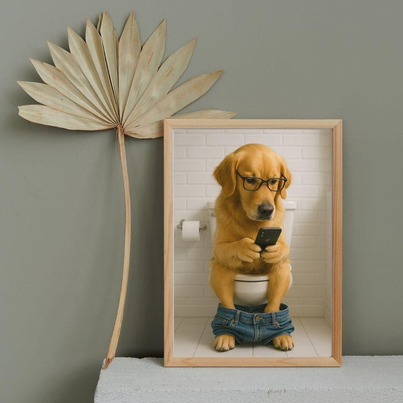 May include: A framed print featuring a Golden Retriever wearing glasses and denim jeans, sitting on a toilet while looking at a smartphone. The background shows a white brick wall and a roll of toilet paper. The frame is made of light-colored wood.