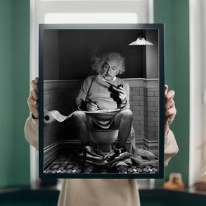 May include: Black and white photograph of Albert Einstein sitting on a toilet, smoking a pipe and writing on a roll of toilet paper.