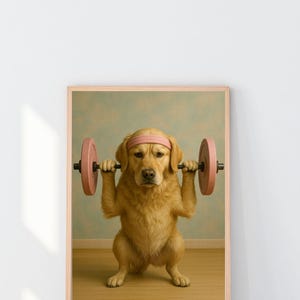 May include: A framed print shows a golden retriever lifting a pink barbell. The dog wears a pink headband and is in a squat. The background is a light blue wall and a wooden floor. The print is in a light brown frame.