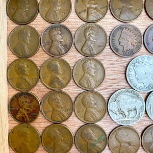 May include: A collection of vintage U.S. coins, including Lincoln pennies and a Buffalo nickel, displayed in a wooden frame. The pennies feature the profile of Abraham Lincoln and various dates, such as 1919, 1936, and 1930.
