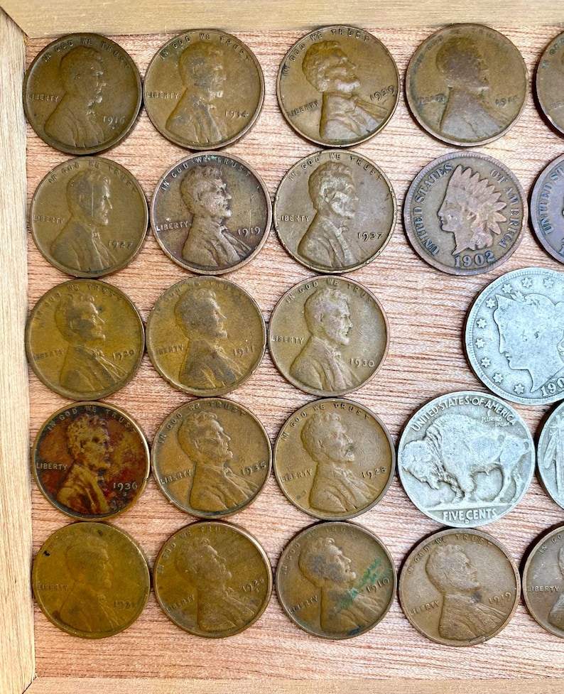 May include: A collection of vintage U.S. coins, including Lincoln pennies and a Buffalo nickel, displayed in a wooden frame. The pennies feature the profile of Abraham Lincoln and various dates, such as 1919, 1936, and 1930.