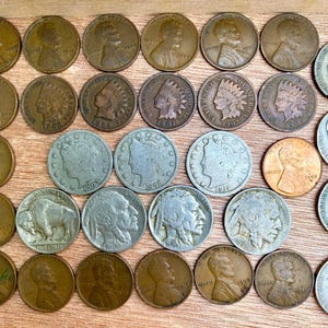 May include: A collection of vintage U.S. coins, including pennies, nickels, and silver coins, arranged on a wooden surface. The coins feature various designs and dates, showcasing American history and numismatics.