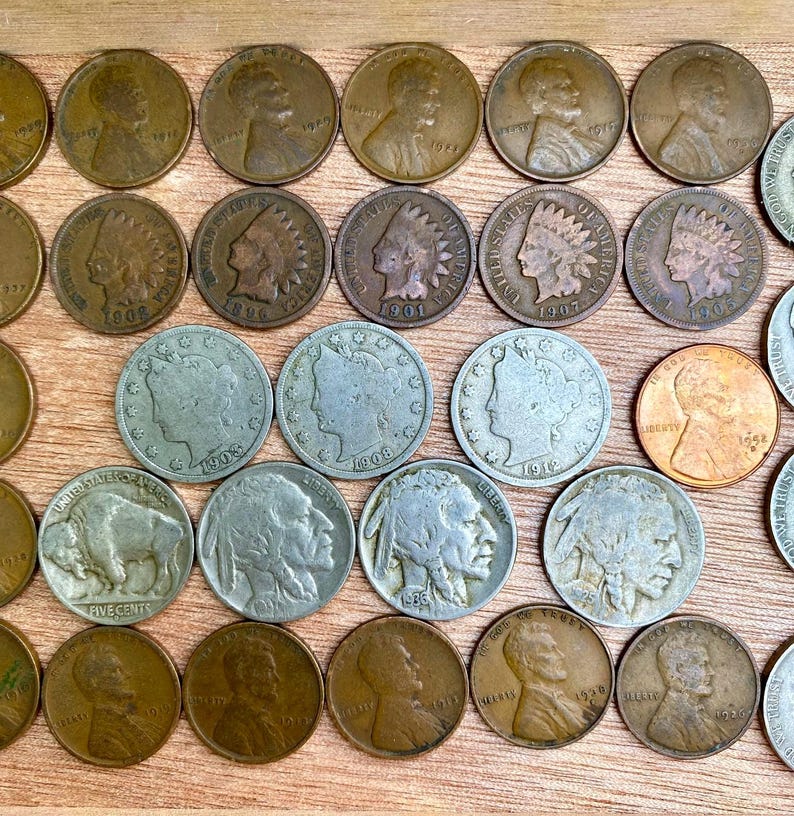 May include: A collection of vintage U.S. coins, including pennies, nickels, and silver coins, arranged on a wooden surface. The coins feature various designs and dates, showcasing American history and numismatics.