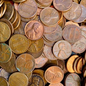 May include: A large collection of copper-colored United States one-cent coins, commonly known as pennies. The coins are scattered in a pile, showing both the profile of Abraham Lincoln and the Lincoln Memorial design on the reverse side.