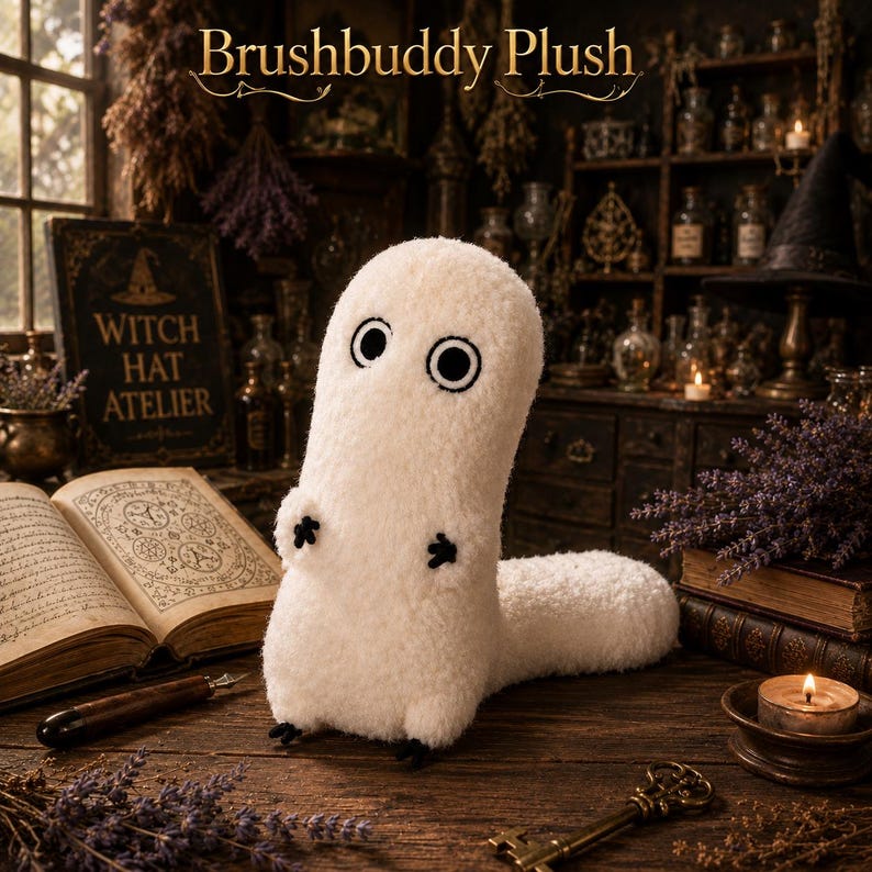 May include: A white, fuzzy, upright plush creature with two large, circular black-and-white eyes and small black stitched hands and feet. The text "Brushbuddy Plush" is displayed above the creature in a decorative, elegant font style.