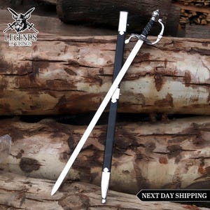 May include: A silver and black rapier sword with a decorative handle and a black sheath. The sword is lying on a wooden surface. The text "Legends of Vikings" is in the upper left corner. The text "NEXT DAY SHIPPING" is in the lower right corner.