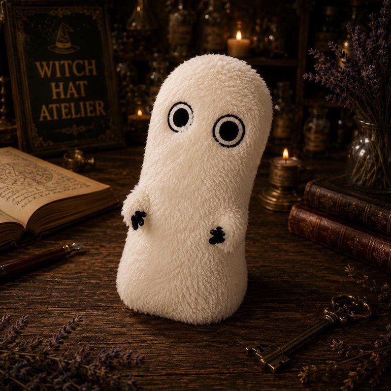 May include: A plush, off-white, fuzzy ghost-shaped figure with two large, circular black embroidered eyes and small, black, three-fingered hands. The soft, textured creature stands upright, featuring a rounded top and a cylindrical body shape.