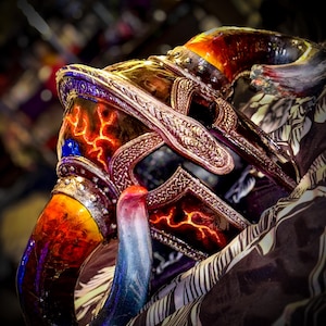 Peut inclure: Gros plan sur une corne décorative aux couleurs dégradées, du rouge au bleu. La corne est ornée de métaux ouvragés et d'un motif rouge flamboyant. L'arrière-plan flou met en valeur le travail artisanal et le design.