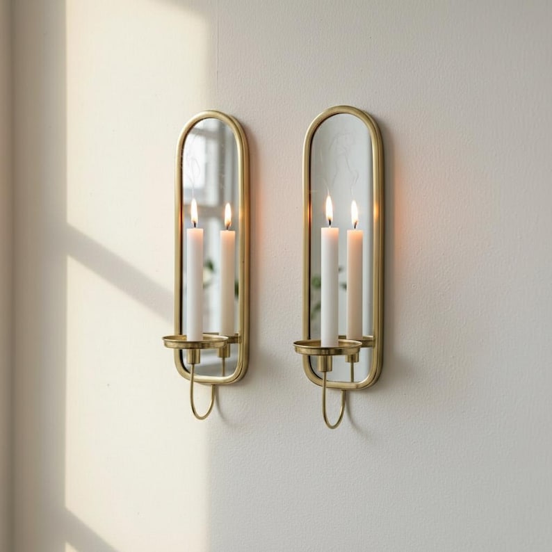 Brass wall candle holders with arched mirrors, displayed with a lit pillar candle and two lit taper candles