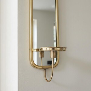 Brass wall candle holders with arched mirrors, displayed with a lit pillar candle and two lit taper candles