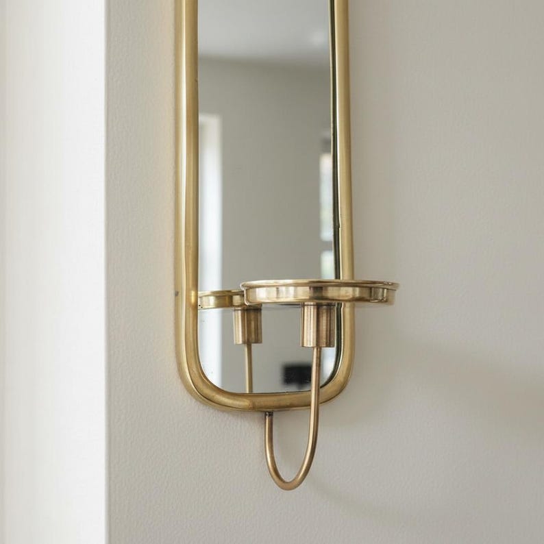 Brass wall candle holders with arched mirrors, displayed with a lit pillar candle and two lit taper candles