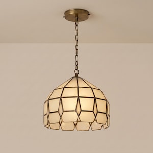 May include: A geometric pendant light. The cream-coloured shade is made up of multiple facets with dark brown outlines. It hangs from a chain and a circular ceiling mount, both in a brass finish. The light is on, illuminating the shade.