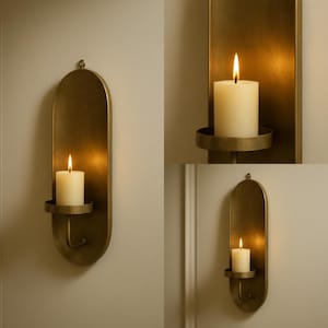 May include: A set of three wall-mounted candle holders in a warm brass finish. Each holder features an oval backplate with a circular candle platform and a lit, ivory-colored pillar candle. The candle flames cast a warm glow.