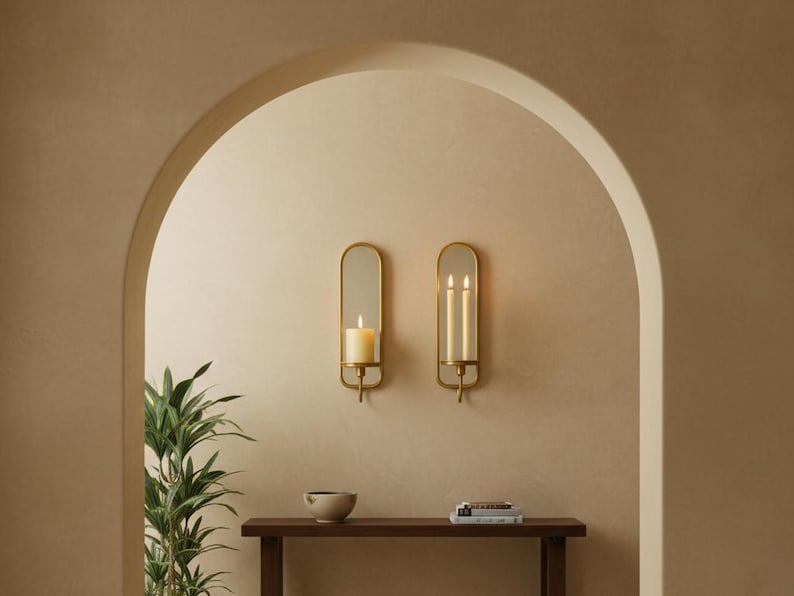 Brass wall candle holders with arched mirrors, displayed with a lit pillar candle and two lit taper candles