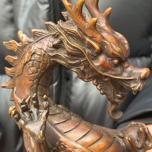 K&ouml;nnte beinhalten: Eine bronzefarbene Drachenskulptur mit aufwendigen Details. Der Drache hat H&ouml;rner, Schuppen und eine geschwungene Haltung. Die Skulptur ist in Bronze- und Braunt&ouml;nen gehalten und zeigt das detaillierte Design der Kreatur.