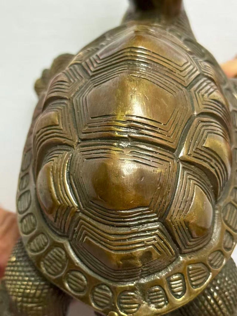 May include: A bronze turtle figurine with a detailed shell pattern. The shell features geometric designs and textured lines, creating a vintage aesthetic. The figurine's color is a mix of bronze and gold.