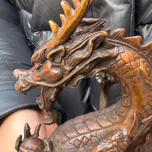 K&ouml;nnte beinhalten: Bronzefarbene Drachenskulptur mit aufwendigen Details. Der Drache hat einen detaillierten Kopf mit Geweih, offenem Maul und Schuppen. Die Skulptur ist ein Dekorationsartikel, wahrscheinlich zur Pr&auml;sentation.