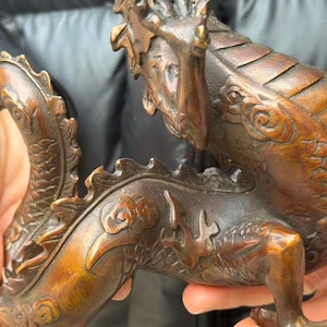 K&ouml;nnte beinhalten: Eine detaillierte Bronzedrachenskulptur mit komplizierten Schuppen und Krallenf&uuml;&szlig;en. Der K&ouml;rper des Drachen ist warmbraun mit dunkleren Akzenten, und es scheint sich um einen dekorativen Gegenstand zu handeln.