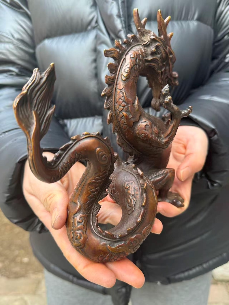 K&ouml;nnte beinhalten: Eine detaillierte Bronzedrachenskulptur. Der Drache ist in einer geschwungenen Pose dargestellt, wobei sein Schwanz und Kopf einen Kreis bilden. Die Skulptur hat eine strukturierte Oberfl&auml;che und eine satte, braune Farbe, die die Schuppen, H&ouml;rner und Krallen hervorhebt.