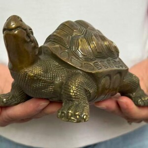 May include: A bronze-colored turtle figurine with detailed shell patterns and textured skin. The turtle is in a walking pose, with its head and legs extended. This decorative item is likely a home decor piece.
