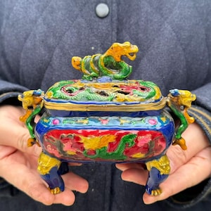 May include: A rectangular cloisonné incense burner featuring a vibrant blue base with red and green dragon motifs. The lid is topped with a sculpted dragon finial, and the vessel is supported by four legs, with two dragon-shaped side handles.