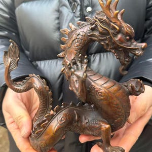 K&ouml;nnte beinhalten: Eine detaillierte Bronzedrachenskulptur. Der Drache ist in einer dynamischen Pose dargestellt, wobei seine Schuppen, Krallen und H&ouml;rner deutlich sichtbar sind. Die Skulptur hat eine reiche, gealterte Patina, was darauf hindeutet, dass es sich um ein antikes oder Vintage-St&uuml;ck handelt.