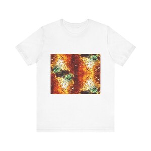 Puede incluir: Una camiseta blanca de manga corta con un estampado gráfico rectangular centrado. El diseño muestra un patrón abstracto en espejo con tonos cálidos de naranja, rojo y amarillo, acentuado por pequeños elementos circulares verdes en la imagen.