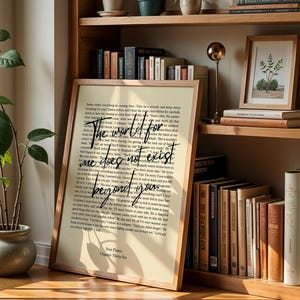 May include: A framed print with the text "The world for me does not exist beyond you" in a handwritten style. The print is in a wooden frame and leans against a bookshelf filled with books.