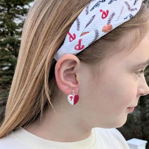 May include: A pair of red and white heart-shaped earrings with a glitter finish. The earrings feature a white heart with a red 'P' in the center and a red heart with white glitter on the other half.