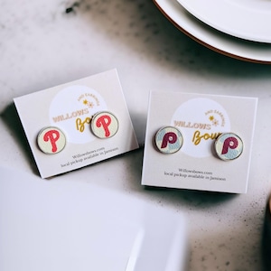 May include: Two pairs of earrings featuring a red and white baseball logo on a cream background. The earrings are displayed on white cards with the text "Willows Bows and Earrings" and "Willowsbows.com local pickup available in Jamison".