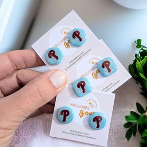 May include: Four pairs of blue and maroon glitter stud earrings with the letter "P" on each earring. The earrings are displayed on white cards with the text "Willowsbows.com local pickup available in Jamison" printed on them.