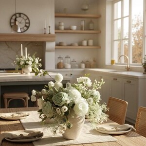 K&ouml;nnte beinhalten: Ein K&uuml;chenessbereich mit einem Holztisch, der f&uuml;r eine Mahlzeit gedeckt ist. Eine Vase mit wei&szlig;en und gr&uuml;nen Blumen steht im Mittelpunkt. Teller, Servietten und St&uuml;hle sind um den Tisch angeordnet. Eine Uhr und Regale sind im Hintergrund zu sehen.