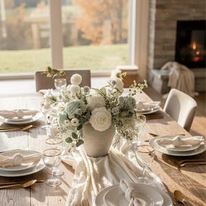 K&ouml;nnte beinhalten: Ein sch&ouml;n gedeckter Esstisch mit einem Blumengesteck. Der Tisch ist aus hellem Holz gefertigt und mit wei&szlig;en Tellern, goldger&auml;nderten Gl&auml;sern und goldenem Besteck gedeckt. Ein wei&szlig;er Tischl&auml;ufer und Servietten vervollst&auml;ndigen das elegante Ambiente.
