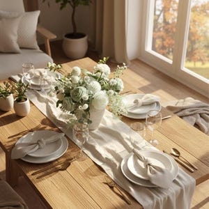 K&ouml;nnte beinhalten: Ein Holztisch, der f&uuml;r eine Mahlzeit gedeckt ist. Der Tisch ist mit wei&szlig;en Tellern, Servietten, goldfarbenem Besteck und Weingl&auml;sern geschm&uuml;ckt. Ein Blumengesteck aus wei&szlig;en und gr&uuml;nen Blumen steht in einer wei&szlig;en Vase. Ein cremefarbener Tischl&auml;ufer sorgt f&uuml;r Eleganz.