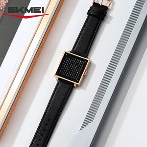 May include: A black leather watch with a square gold-colored face. The watch face displays a grid of letters. The watch band is black leather with a gold-colored buckle. The brand name "SKMEI" is visible in the top left corner.