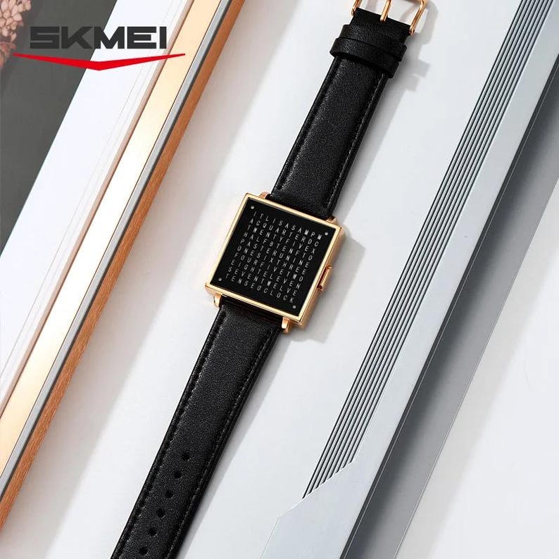 May include: A black leather watch with a square gold-colored face. The watch face displays a grid of letters. The watch band is black leather with a gold-colored buckle. The brand name "SKMEI" is visible in the top left corner.