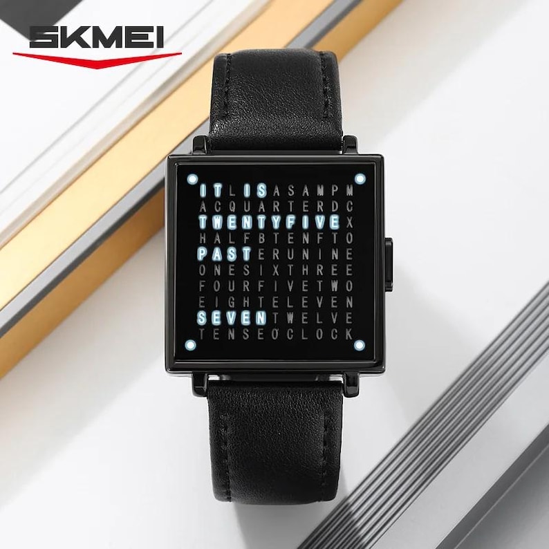 May include: Black square-faced watch with a black leather band. The watch face displays the time using words. The brand name "SKMEI" is in the upper left corner. The watch band is 9 inches long.